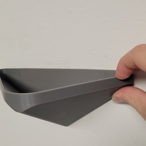 Puede incluir: Un estante de pared de plástico gris con forma triangular.