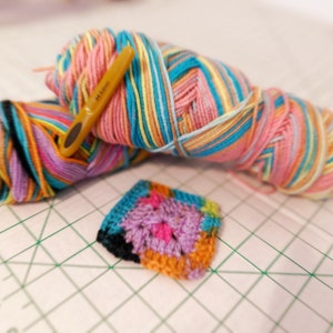 May include: Two balls of colorful yarn, one pink, blue, yellow, and white, and the other purple, orange, black, and white, with a yellow crochet hook.