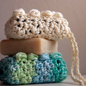 Puede incluir: Un conjunto de tres jaboneras de ganchillo en blanco, verde y azul. Las jaboneras están hechas de hilo de algodón y tienen un diseño texturizado y tejido. Las jaboneras están apiladas una encima de la otra, con la jabonera blanca en la parte superior.