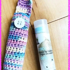 May include: A crocheted, multi-coloured pouch with a white button, holding a small tube of coconut lip balm. The lip balm tube is white with blue and gold text that reads "COC organic lip balm virgin coconut oil" and "Net Wt. 0.15oz/4.25g NUTRITIOUS, MEAN".