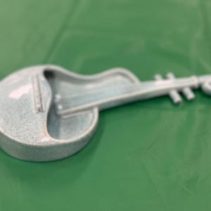 May include: A light blue ceramic violin shaped dish. The dish is on a green surface.