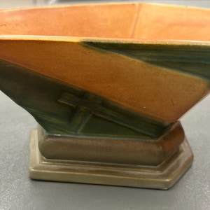 May include: A brown and green ceramic planter with a geometric design. The planter has a wide, shallow bowl and a square base.