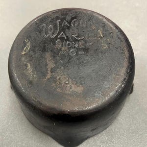 May include: Black cast iron pot with the text "Wagners Ware Sydney" and the number "1368" on the bottom.