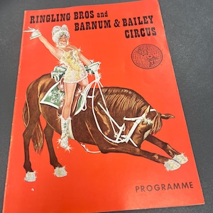 May include: A red and white program for the Ringling Bros. and Barnum & Bailey Circus. The cover features a woman in a sparkly costume riding a brown horse. The text "The Greatest Show On Earth" is in a circle on the cover.