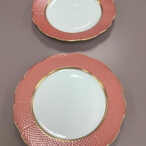 May include: Two pink and white ceramic dinner plates with a gold rim. The plates have a textured surface and a scalloped edge.