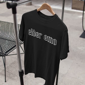 May include: Black t-shirt with white text that reads "elder emo" in a gothic font.