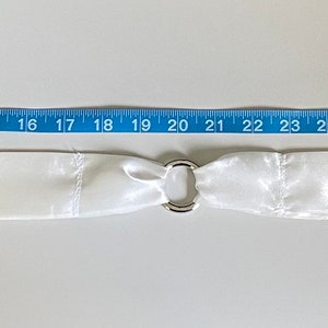 Puede incluir: Una faja de sat&eacute;n blanco con una hebilla plateada. La faja mide 104 cm de largo.