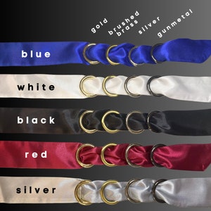 Puede incluir: Cinco cintas de sat&eacute;n de diferentes colores, azul, blanco, negro, rojo y plateado, con anillos de oro, lat&oacute;n cepillado, plata y metal gris unidos a cada cinta.