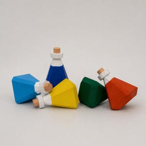May include: A collection of colorful, geometric wooden potion bottles. The bottles are painted in blue, yellow, green, and red, with white and cork stoppers. The bottles are arranged on a white surface.