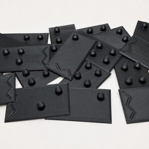 May include: A collection of black, rectangular objects with rounded protrusions. Each piece has a unique zig-zag design on one edge. The objects are scattered on a white surface, creating a visually interesting arrangement.