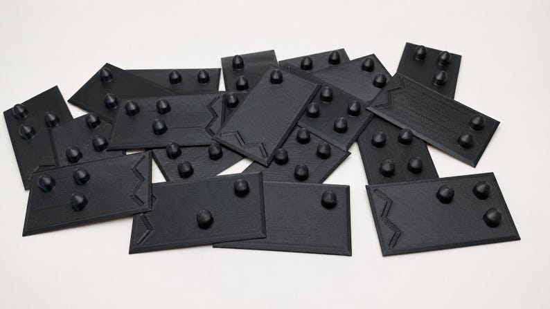 May include: A collection of black, rectangular objects with rounded protrusions. Each piece has a unique zig-zag design on one edge. The objects are scattered on a white surface, creating a visually interesting arrangement.