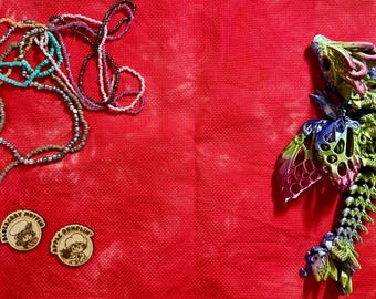 May include: A collection of multi-colored beaded necklaces, two circular wooden tokens featuring engraved characters and the text Blueberry Muffin and Apple Dumplin, and a multi-colored articulated dragon figure with green, blue, and purple tones.