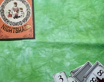 May include: A bright green fabric with a mottled texture. In the top left corner, a rectangular card features a circular illustration of three glass bottles and the text NIGHTSHADE. In the bottom right, several playing cards are visible.
