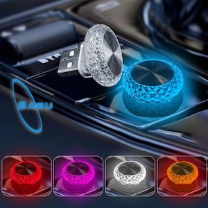 Puede incluir: Un cargador de coche USB con un diseño de corte de diamante y una luz azul brillante. La imagen muestra el cargador en varios colores, incluyendo rojo, morado, blanco y naranja. La palabra "SARU" está escrita en azul.
