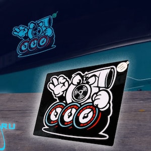 Pode incluir: Adesivo preto e branco de um turbocompressor de desenho animado com três medidores. O turbocompressor tem um grande tubo de escape e está usando uma expressão travessa. O adesivo está em um fundo preto.