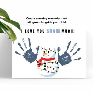 May include: A white card with a blue snowman wearing a red scarf and a string of colorful lights. The snowman is surrounded by two blue handprints. The card says "I LOVE YOU SNOW MUCH!"