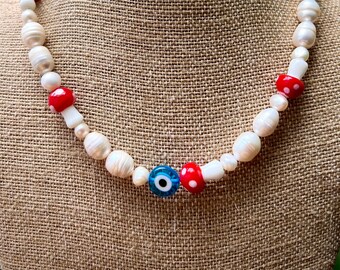 Könnte beinhalten: Eine weiße Perlenkette mit roten und weißen Tupfenperlen und einem blauen bösen Blick-Anhänger.