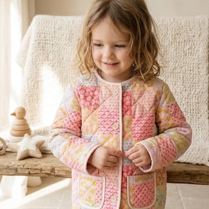 May include: A quilted jacket in a patchwork design with pink, yellow, and white squares. The jacket has two pockets and is buttoned up. The jacket is worn by a young child.