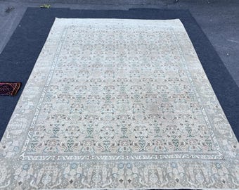 May include: Large, rectangular, beige rug with an intricate floral pattern in shades of blue, green, and peach. The rug has a detailed border and a smaller, patterned rug is visible in the corner. The rug is placed on a dark blue surface.