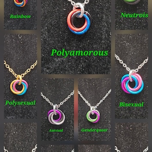 May include: A collection of necklaces with interlocking rings in various colors, each suspended from a delicate chain. The necklaces represent different identities, with text labels such as "Rainbow," "Bisexual," and "LGBTQIA+".