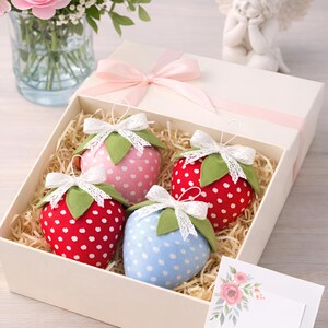 Fabric strawberry sewing pattern gift box with handmade plush berries in different colors, lace bows and greeting card on table with flowers
