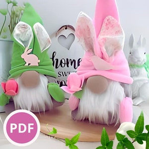 Może przedstawiać: Dwa gnomy wielkanocne, jeden zielony, a drugi różowy, z uszami króliczka i kwiatami. Gnomy siedzą na drewnianej powierzchni z zielonymi roślinami w tle. Tekst "PDF" znajduje się na różowym kółku na pierwszym planie.