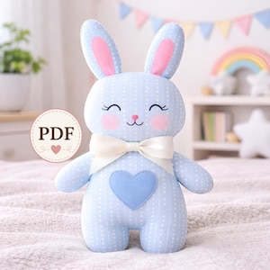 Può includere: Un coniglietto di peluche azzurro con pois bianchi, interno orecchie rosa e un fiocco color crema. Il coniglietto ha un cuore blu sulla pancia e un viso sorridente con guance rosee. L'immagine include un logo "PDF".
