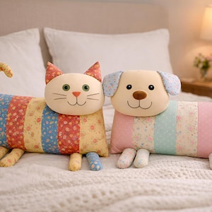 May include: Two soft toy animal cushions: a cat and a dog. The cat has a cream face, green eyes, and a striped body in red, blue, and yellow floral patterns. The dog has a cream face, brown nose, and a body in pink, blue, and yellow floral patterns.