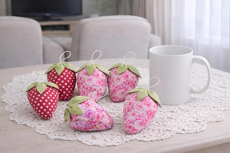 Pink and red fabric strawberry ornaments styled on lace tablecloth with cup in cozy living room