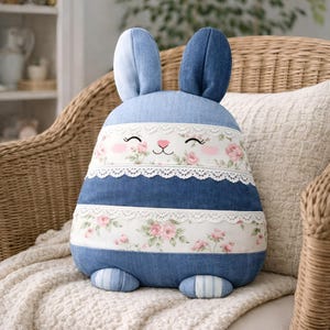 Blue bunny pillow with lace stripes placed on a wicker chair.