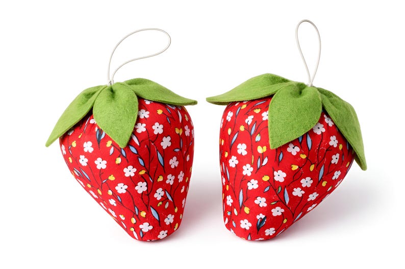 Pair of small red plush strawberries with hanging loops and lace bows isolated on white