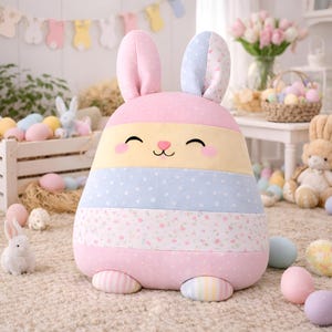 Pink bunny pillow with soft striped body and pastel Easter decorative details.