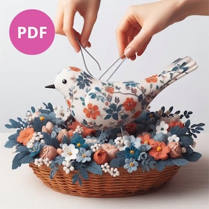 Puede incluir: Un pájaro de fieltro hecho a mano con un patrón floral se sienta en una cesta tejida llena de flores de fieltro en tonos azules, blancos y naranjas.