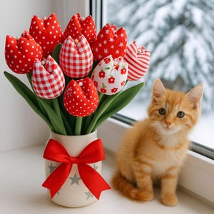 Op de afbeelding: Een boeket stoffen tulpen met rode en witte patronen, waaronder stippen, ruitjes en bloemmotieven. De crèmekleurige vaas is versierd met een rode strik. Een oranje katje zit naast de vaas. De vensterbank toont een besneeuwde landschap.