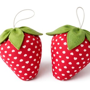 Two small red plush strawberry ornaments with lace bows and felt leaves isolated on white background