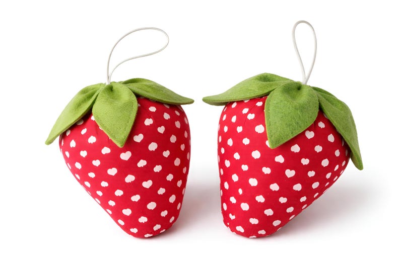 Two small red plush strawberry ornaments with lace bows and felt leaves isolated on white background