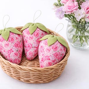 Wicker basket filled with pink strawberry ornaments with lace bows styled with flowers on table