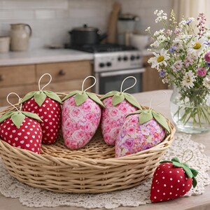 Basket with handmade pink fabric strawberries with lace bows on table in cozy kitchen interior