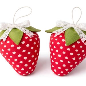 Two red plush fabric strawberries with white heart print and lace bows isolated on white background