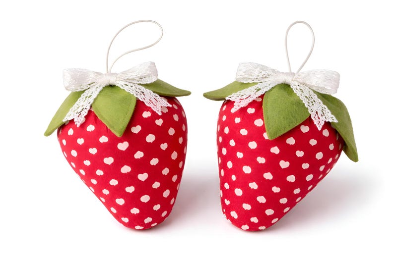 Two red plush fabric strawberries with white heart print and lace bows isolated on white background