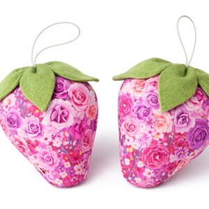 Two pink fabric strawberry ornaments with green felt leaves and lace bows isolated on white