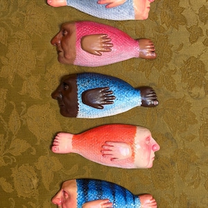 May include: Five sculpted figures shaped like fish with human heads, hands, and feet. Each figure features a unique color scheme including grey, pink, blue, orange, and striped blue, with detailed skin tones and textured scales on the bodies.