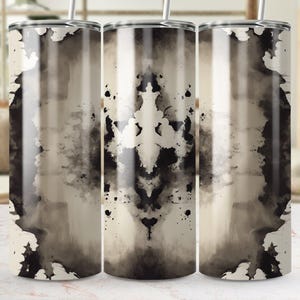 May include: Three stainless steel tumblers with a black and white abstract ink blot design. The design is symmetrical and resembles a Rorschach inkblot test.