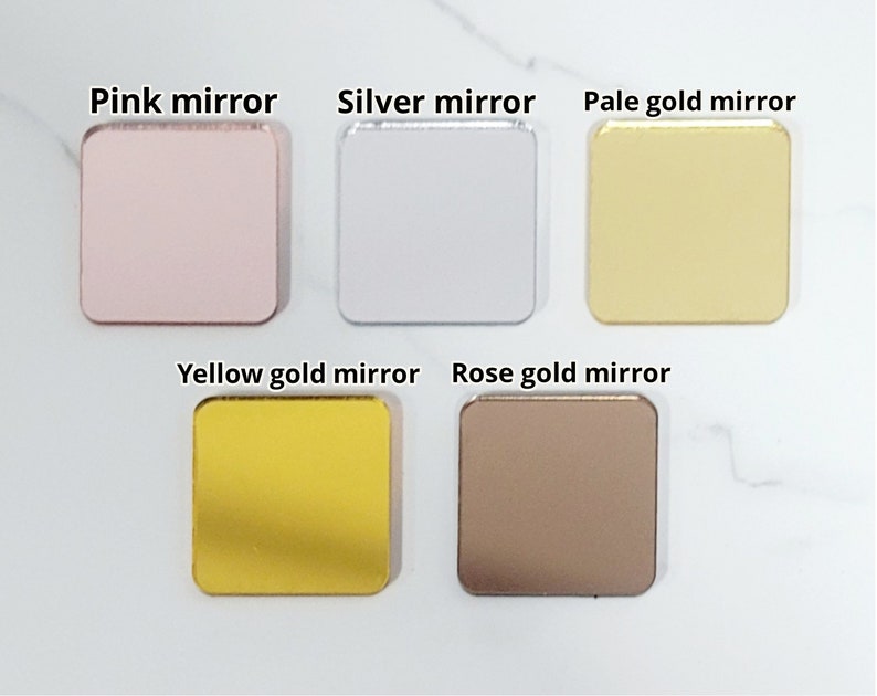Puede incluir: Cinco espejos cuadrados de diferentes colores: rosa, plata, oro p&aacute;lido, oro amarillo y oro rosa. Los espejos est&aacute;n dispuestos en dos filas sobre una superficie blanca.