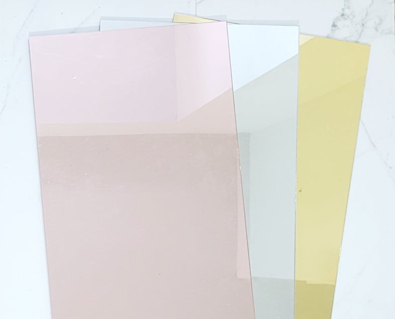 Puede incluir: Cuatro hojas de papel decorativo en diferentes colores. Las hojas est&aacute;n apiladas una encima de la otra. La hoja superior es rosa, la segunda hoja es blanca, la tercera hoja es gris claro y la hoja inferior es dorada.