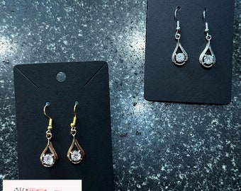 May include: Two pairs of dangle earrings with a clear crystal stone in the center. The earrings are on black card stock with the text "MJ's Jewellery Handmade Jewellery".