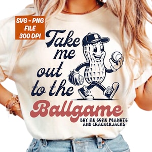 May include: Cream-colored t-shirt featuring a cartoon peanut character wearing a baseball cap and holding a baseball. The shirt has the text "Take me out to the Ballgame" in navy and burgundy, with additional text below.