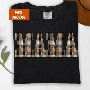 Könnte beinhalten: Schwarzes T-Shirt mit dem Wort "MAMA" in großen Blockbuchstaben. Die Buchstaben sind mit einem Patchwork-Design aus Karomustern und Leopardenmuster gefüllt. Das Shirt hat ein Comfort Colors-Etikett.