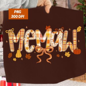 May include: A brown textile featuring the word "MOMAW" in a fall-themed design. The letters are decorated with plaid, floral patterns, and bows. Pumpkins and leaves accent the design. The top left corner has a "PNG 300 DPI" label.