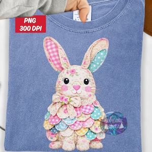 Könnte beinhalten: Hellblaues T-Shirt mit einem bunten Hasen-Design. Der Hase hat rosa und weiß karierte Ohren, ein florales Gesicht und einen geschichteten Rock aus verschiedenen gemusterten Stoffen. Der Text "PNG 300 DPI" befindet sich in der oberen linken Ecke.